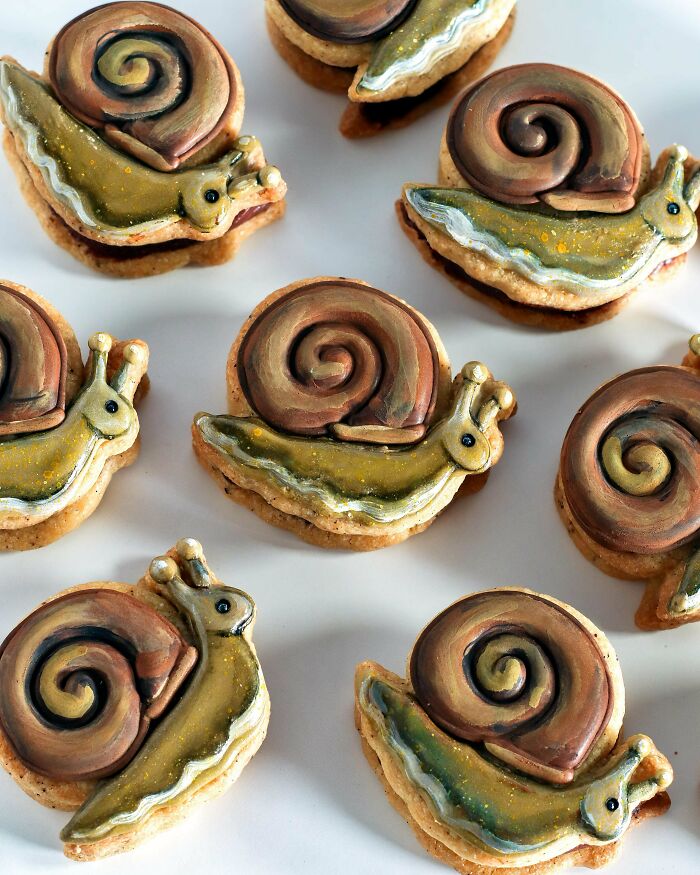 Snail shaped cookies with detailed icing and vibrant colors, showcasing incredible bakes with artistic decoration on a white surface.