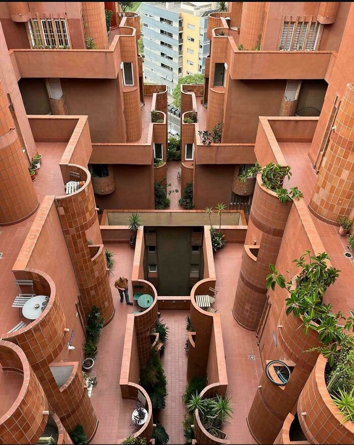 Impressive architectural feats in a terracotta building with curved balconies, plants, and geometric design elements.