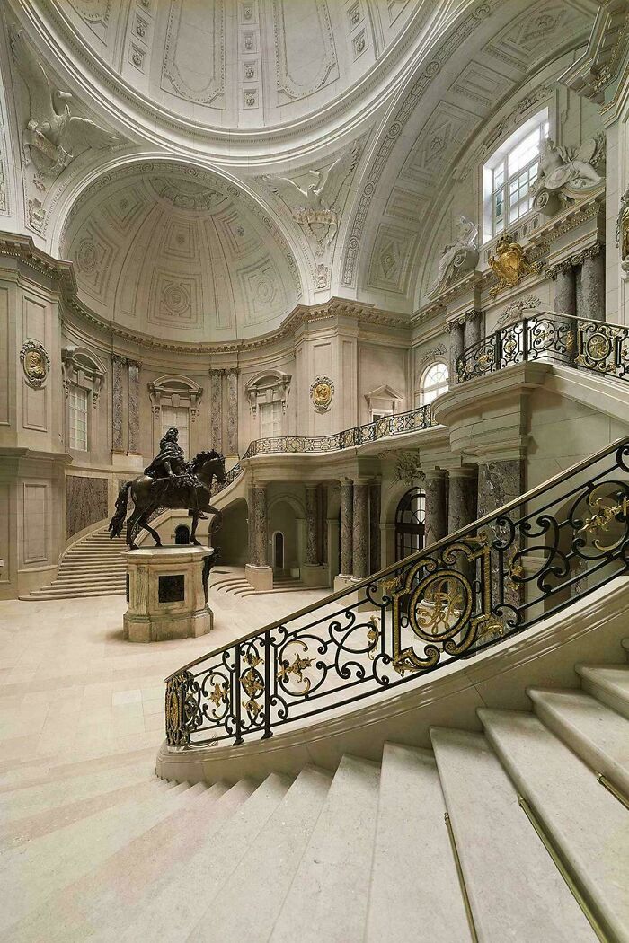 Grand staircase in a historic building featuring impressive architectural feats with ornate railings and a central equestrian statue.