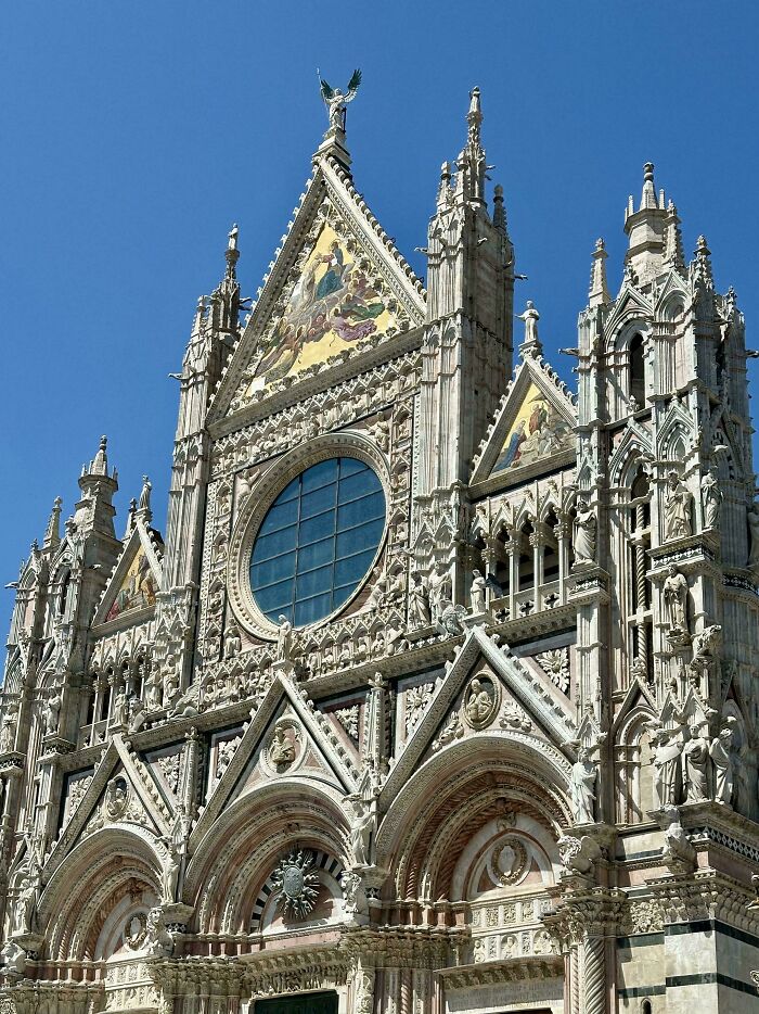 Gothic cathedral facade showcasing impressive architectural feats with detailed sculptures and ornate design under clear blue sky.
