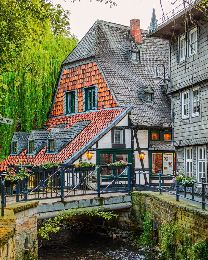 Charming historic building with unique architectural feats featuring intricate roof design and a small stone bridge over water.