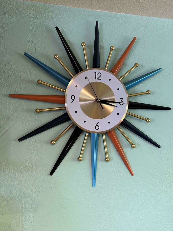 Vintage sunburst wall clock with blue, orange, and black rays, a standout thrift store find hanging on a textured green wall.