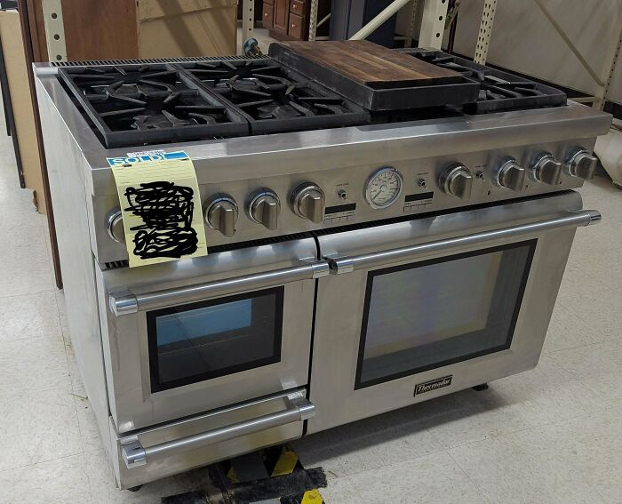 Stainless steel gas range stove with dual ovens and wooden cutting board on top, a rare thrift store find.