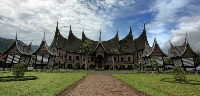 Traditional evil building with sharp, pointed roofs and dark wooden structure under a cloudy sky in a green landscape.