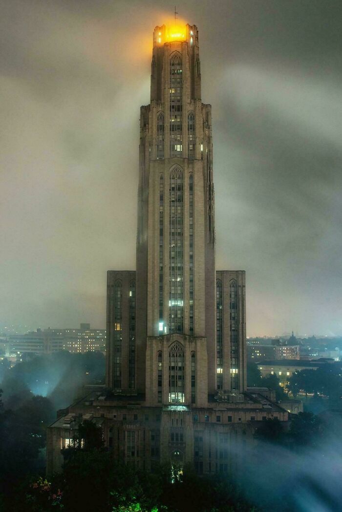 Tall evil building with gothic architecture glowing at the top surrounded by fog in an eerie nighttime cityscape