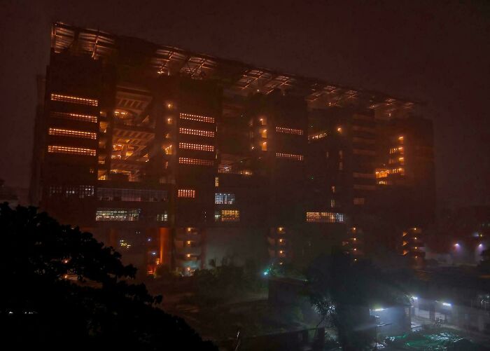 Evil building with dim orange lights glowing through windows, creating a horror movie atmosphere on a foggy night.