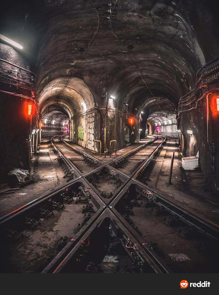 Dark underground train tunnels with intersecting tracks and eerie red lights in an evil building setting.