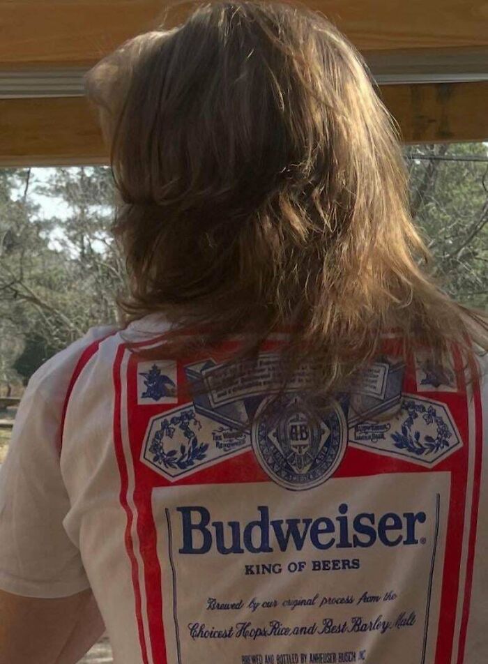 Man with fierceflow beautiful hair standing outdoors wearing a vintage Budweiser t-shirt in natural light