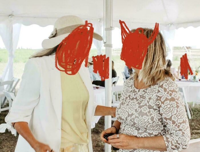 Two women at a wedding tent, one in a white blazer and hat, the other in a lace dress, capturing awkward wedding moments.