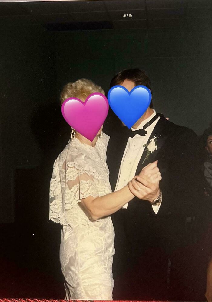 Bride and groom dancing at wedding, dressed in vintage attire, with faces covered by heart emojis, wedding guests in background.