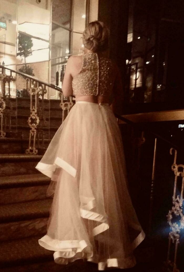 Woman wearing a beaded top and sheer wedding skirt walking up stairs in an awkward wedding moment shame online.