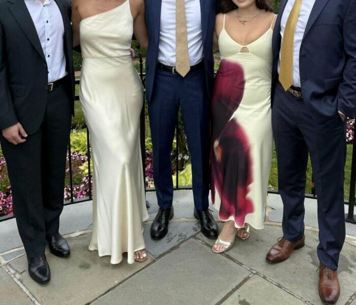 Two women in cream-colored dresses and three men in suits stand together at a wedding moment with an unusual dress stain.