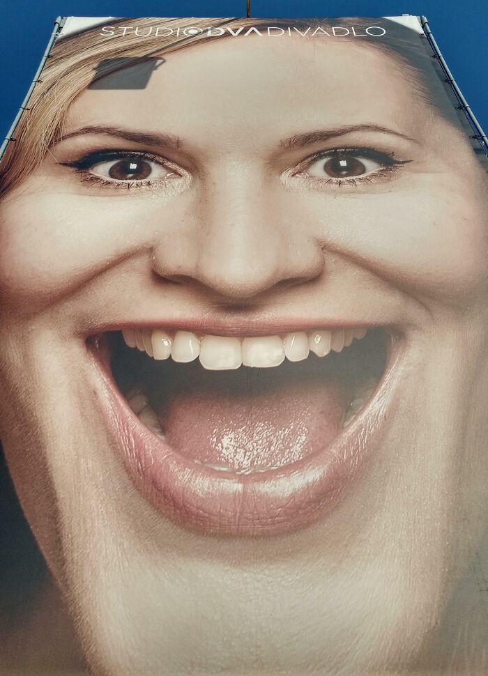 Gigantic distorted smiling face on an outdoor advertising banner showing unattainable body portrayal in advertising fails.