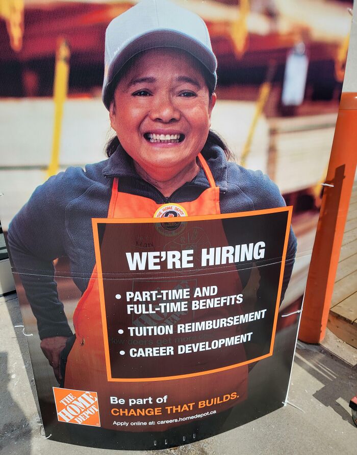 Smiling employee in an orange apron holding a hiring sign with benefits, part-time, tuition, and career development offers.