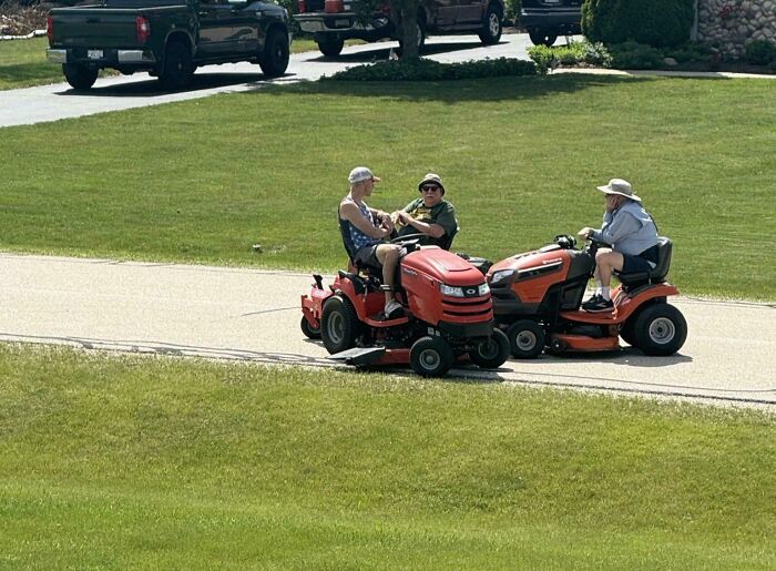 Three dads on riding lawnmowers chatting on a sunny day, showcasing hilarious dads nailing fatherhood with fun moments.