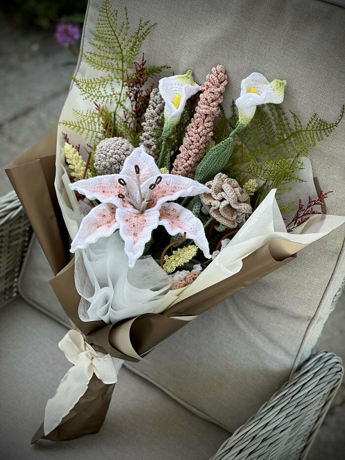Crochet enthusiasts crafted an intricate bouquet of lifelike flowers wrapped in brown and white paper on a chair.