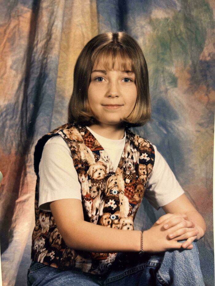 Young girl posing in a regrettable past photo, wearing a dog print vest and casual jeans, sitting with folded hands.