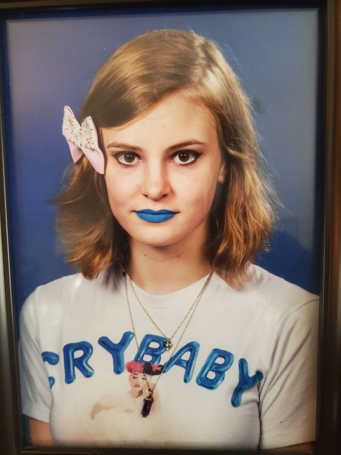Portrait of a young woman with blue lipstick, a bow in her hair, and a crybaby shirt reflecting a regrettable past cringe moment.