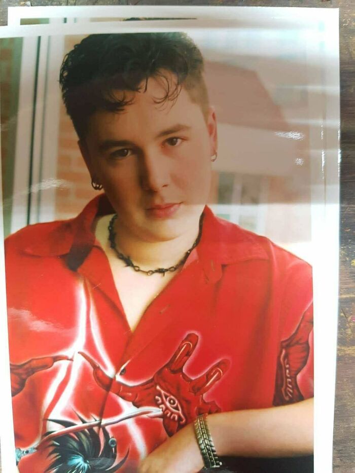 Young man in a red graphic shirt and chain necklace posing for a photo from his regrettable past that causes cringe now.