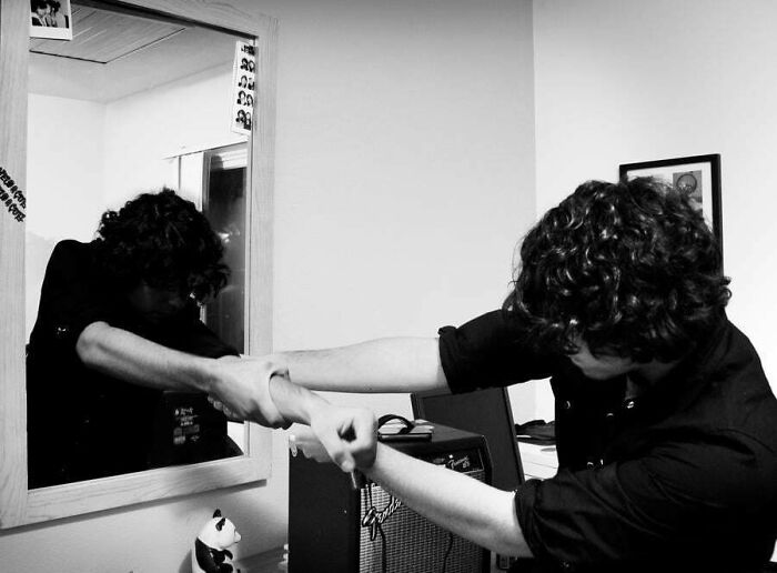 Person with curly hair pulling their reflection’s arm in a black and white image from a regrettable past photo.