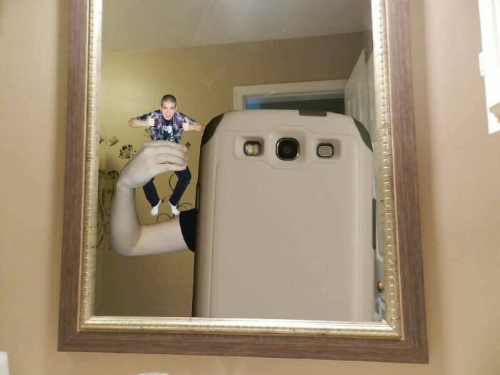 Person taking a mirror selfie holding a tiny edited image of themselves floating above their hand as a regrettable past pic.