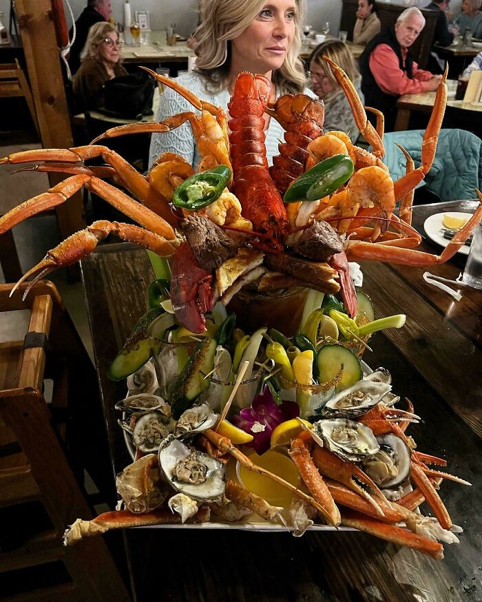 Overloaded seafood platter with crab legs, lobster, shrimp, oysters, and jalapenos in a busy restaurant setting.
