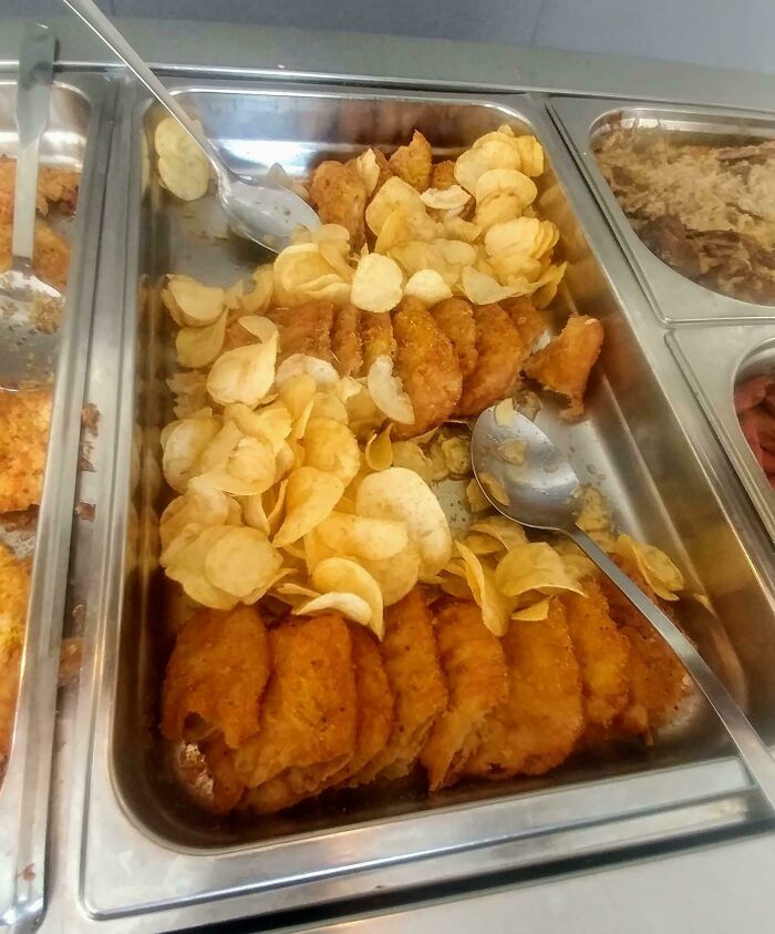 Fried fish fillets served in a buffet tray with potato chips, an unusual combination of dishes in a food display.