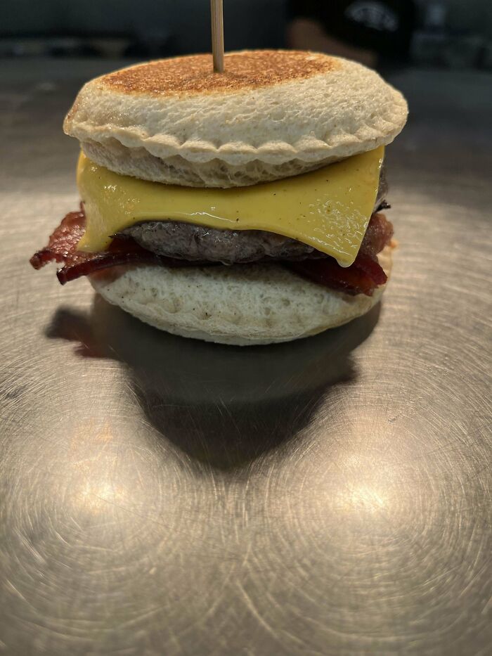 Unusual dish featuring a sandwich with a crispy pie crust bun, cheese, bacon, and beef patty on a metal surface.
