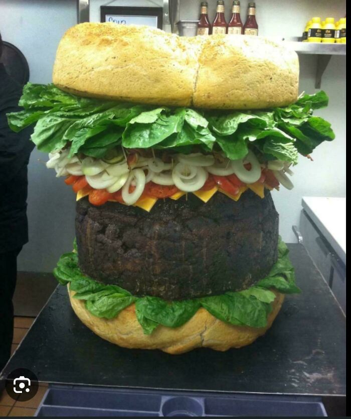 Gigantic burger with oversized lettuce, onions, cheese, and thick patty showcasing unusual dish creativity and size.