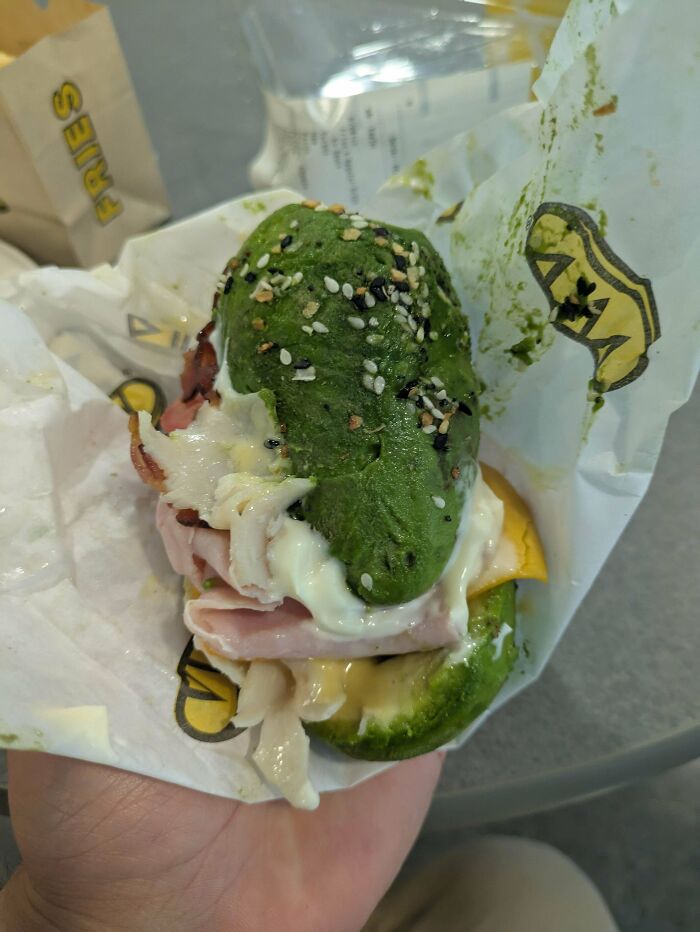 Green seeded sandwich bun with ham, cheese, and sauce held in hand as part of unusual dishes that are just stupid.