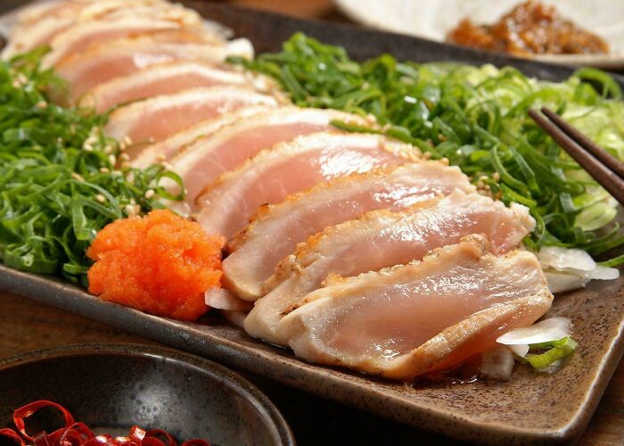 Sliced raw chicken dish served with greens and spicy condiments, showcasing one of the most unusual dishes.