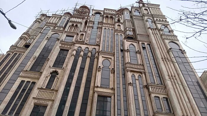 Tall bizarre building with unique architectural details and ornate windows against a gray sky background.