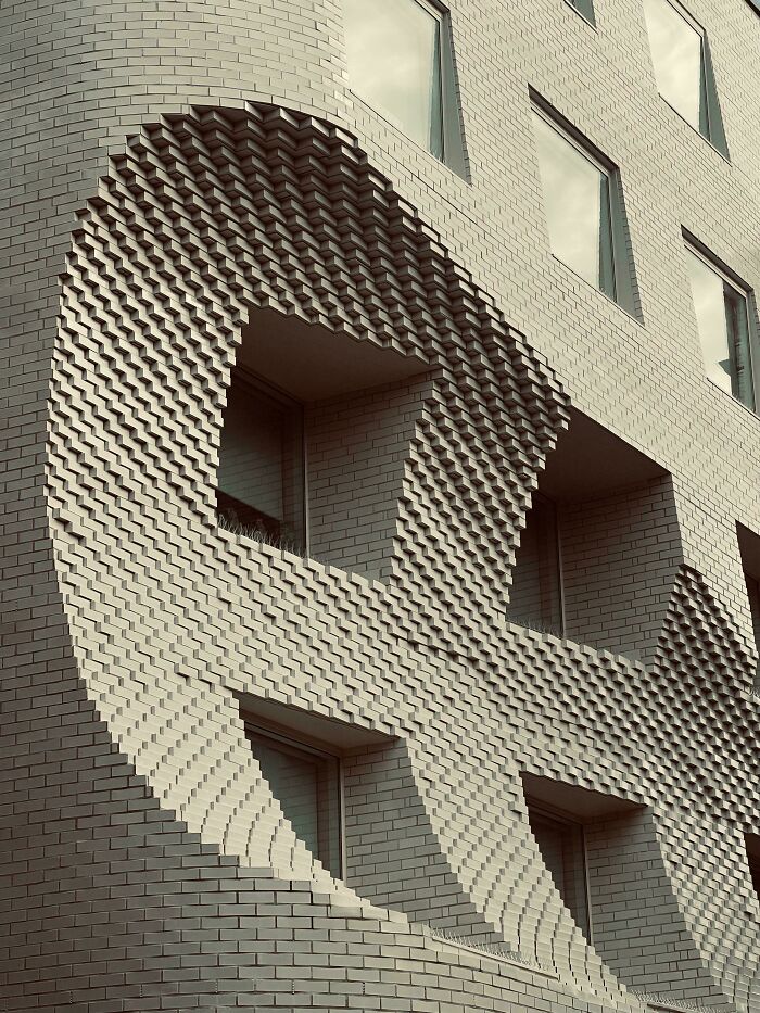 Facade of a bizarre building with unique brick pattern creating a 3D optical illusion around windows in modern architecture.