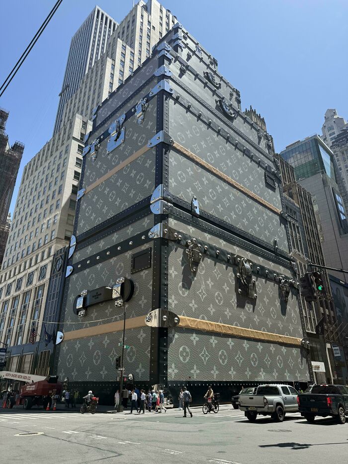 Bizarre building designed as a giant luxury trunk with detailed hardware and patterns in a busy city intersection.