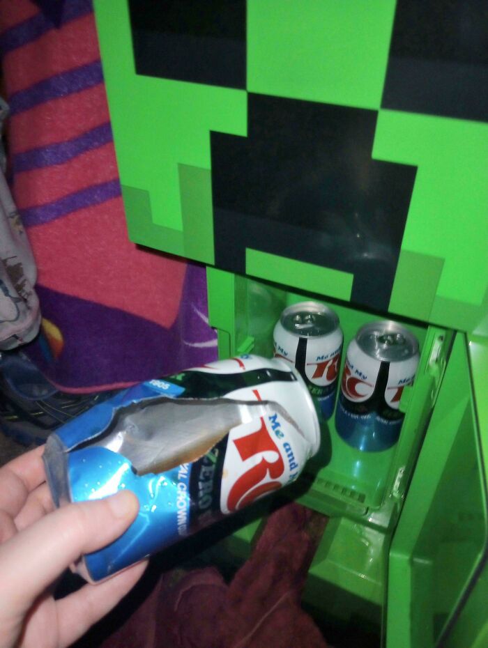 Hand holding a crushed soda can reflected perfectly in a Minecraft-themed mirror, showing a coincidence captured in a photo.
