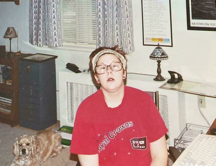 Person in oversized glasses and red shirt sitting indoors with a dog, capturing a regrettable past cringe moment photo.