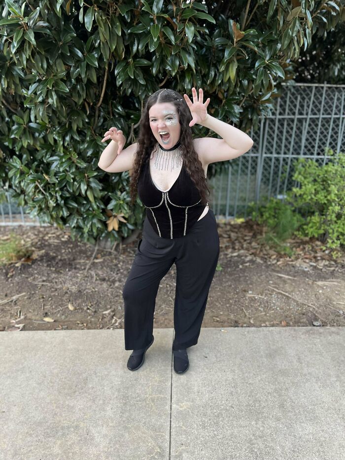 Young woman posing with playful growl in black outfit outdoors, capturing a moment from her regrettable past photos.