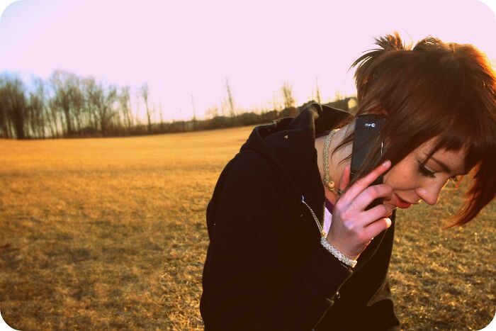 Young woman in a black hoodie outdoors, smiling while talking on the phone, reflecting on a regrettable past moment.