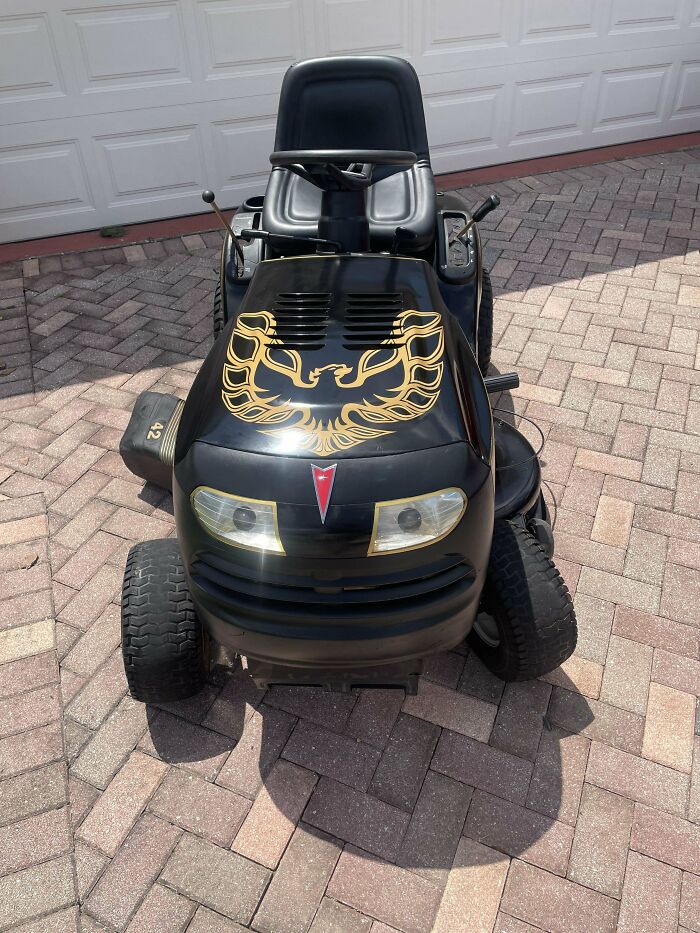 Black riding lawn mower with gold bird decal on hood, demonstrating redneck engineer ingenuity and creativity outdoors.