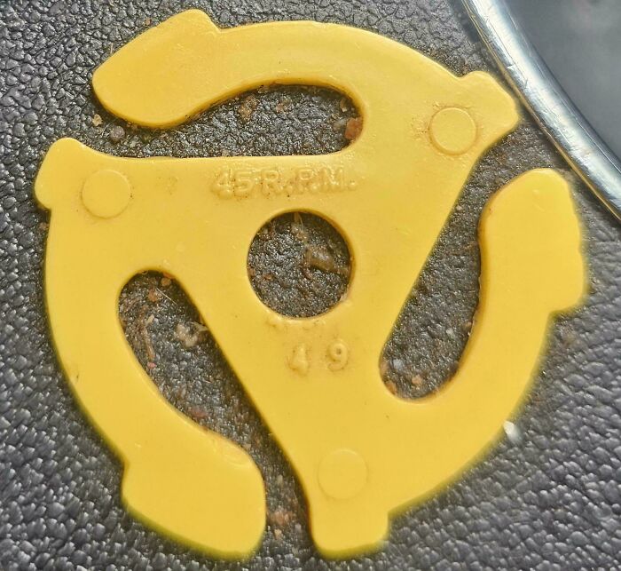 Yellow 45 RPM vinyl record adapter on textured black surface, a nostalgic item that makes people who recognize it feel very old.