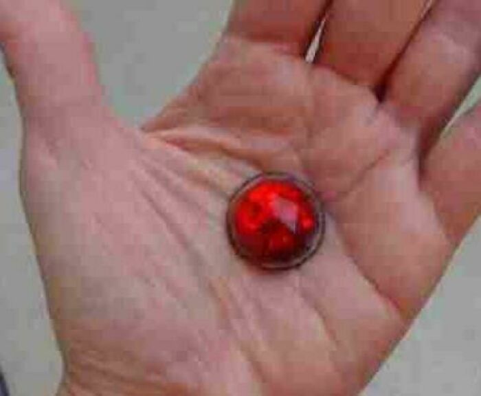 Hand holding a vintage red marble, one of the nostalgic things that make people who recognize them feel very old.