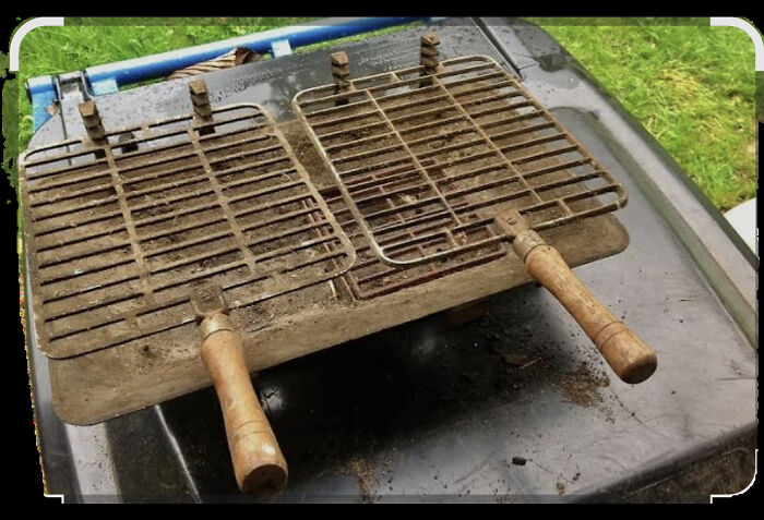 Old rusty vintage grilling racks with wooden handles placed on a black surface, evoking nostalgia and memories.