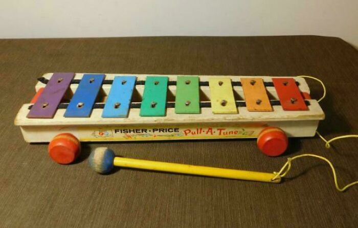 Vintage Fisher-Price Pull-A-Tune xylophone toy with colorful metal keys and wooden mallet on brown surface, nostalgic childhood item.
