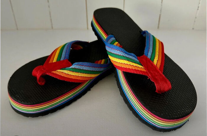 Pair of black flip-flops with rainbow-striped straps and soles, a nostalgic item that makes people who recognize them feel very old.