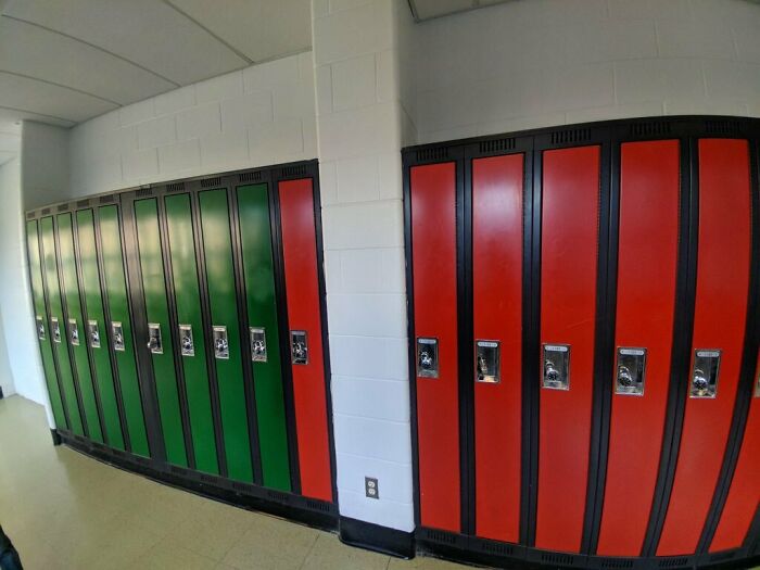 A row of school lockers with mostly green doors and a few red ones, showing imperfect alignment that may annoy people.