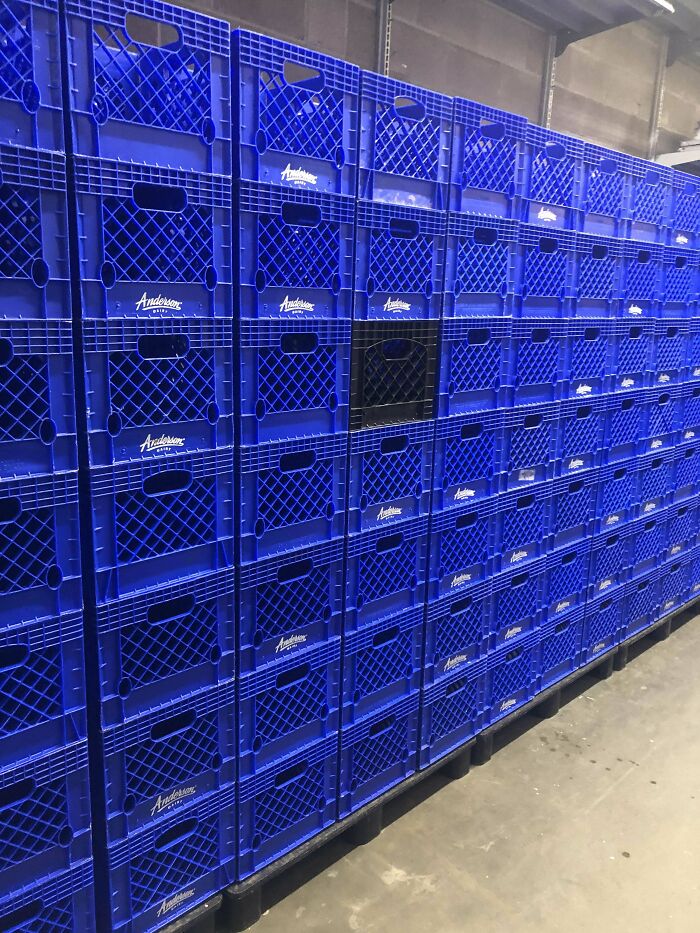Rows of blue plastic crates stacked neatly with one black crate disrupting the perfect pattern, not for you if you have OCD.