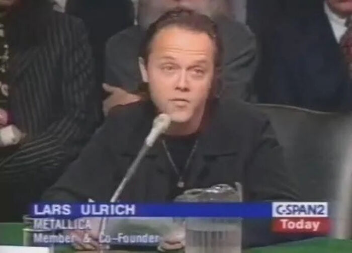 Man speaking into microphone at a panel discussion, part of an online group sharing interesting facts and pics.