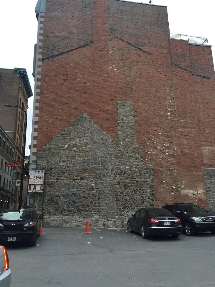 Old stone wall outline visible under newer brick wall in urban parking lot, shared by online group interesting facts.