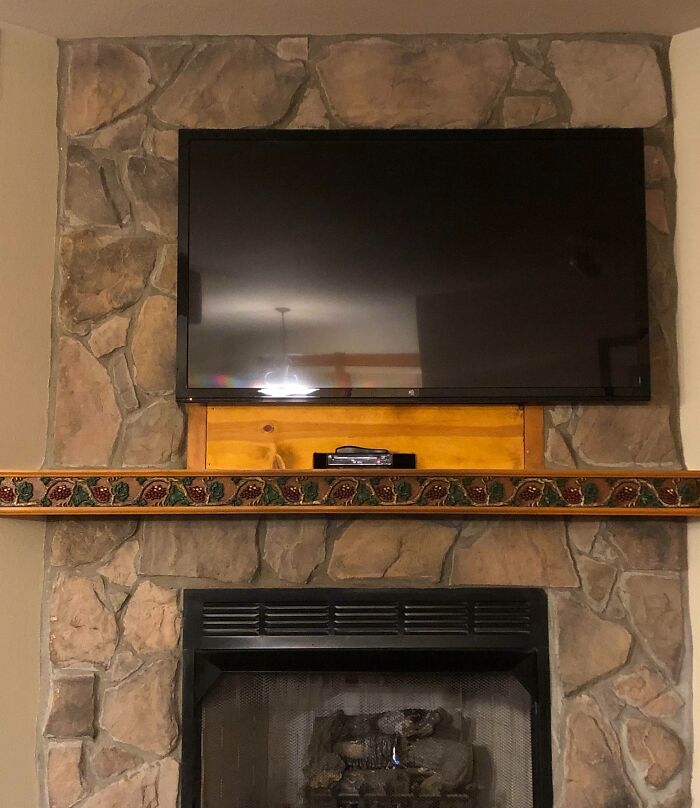 Stone fireplace with a mounted flat screen TV, wooden mantel, and a small electronic device below the television.