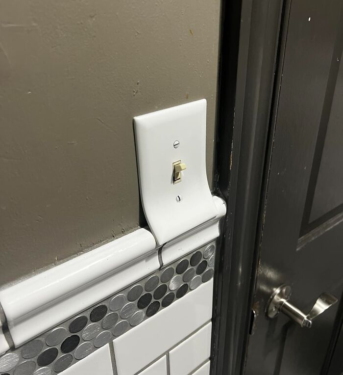 Light switch plate warped and misaligned above imperfect tile grout and door frame, showing common OCD annoyances.